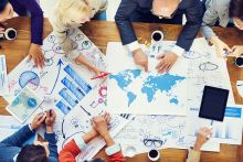 People around a table, photo is taken from above, they're looking at a map of the world